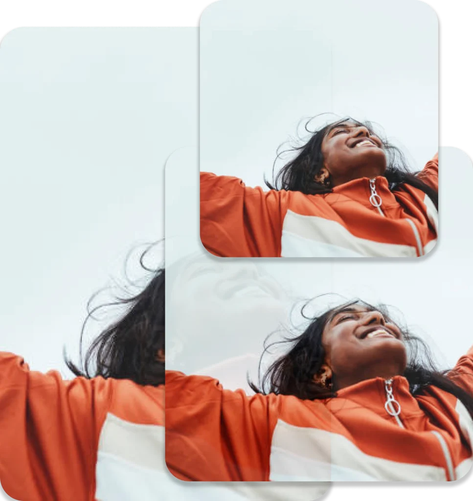 A person in a bright orange jacket with white accents joyfully looks upward, arms outstretched against a cloudy sky.