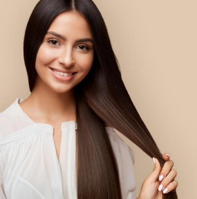 Woman with long, sleek hair is gently holding a strand, wearing a white blouse against a soft, neutral background.